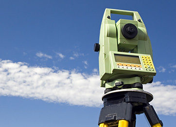 Here's an alt tag for the image: `Surveyor's theodolite against a blue sky.`